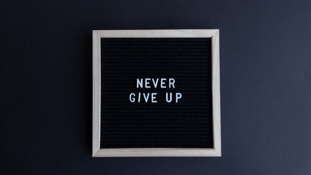 Inspirational letter board with 'Never Give Up' phrase on gray background.