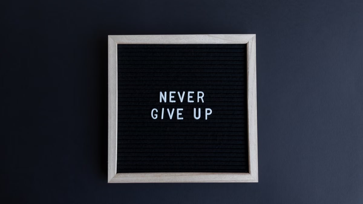 Inspirational letter board with 'Never Give Up' phrase on gray background.